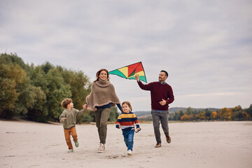 Playful family flying kite in autumn day on lake shore.