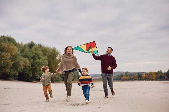 Playful family flying kite in autumn day on lake shore.