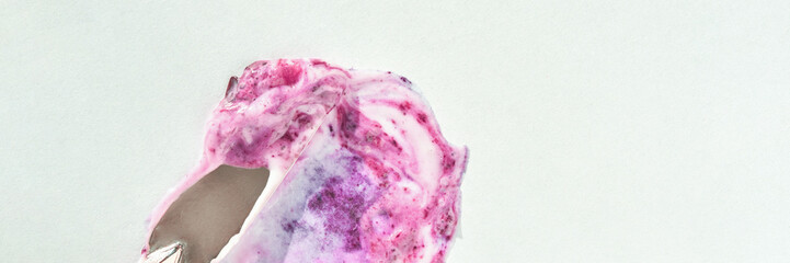 Close-up of pink and purple berry yogurt swirl on white background with spoon.