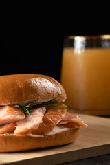 A sandwich with salmon and dill is sitting on a wooden cutting board next to a glass of juice