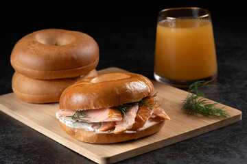 A sandwich with salmon and dill is on a wooden board next to a glass of juice. The sandwich is cut in half and placed on top of another half