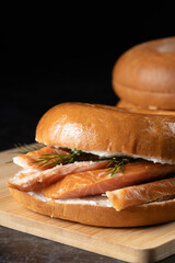 A sandwich with salmon and dill on top of a bun. The sandwich is sitting on a wooden cutting board