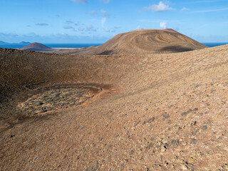 Aerial view of volcanic cones and arid terrain on La Graciosa Island near Lanzarote, with the Atlantic Ocean in the background.
