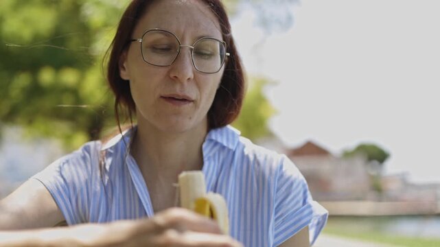 Woman with glasses eating banana outdoors
