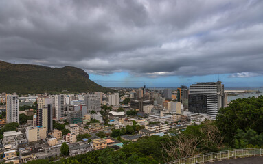 Panoramic view of Port Louis, the capital city of Mauritius, with a dramatic mountain range in the background under moody skies. This urban landscape highlights the contrast 