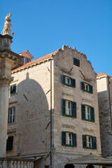 A historic stone building with traditional green shutters in the old town of Dubrovnik, Croatia. The shadow of a dome falls across the facade.