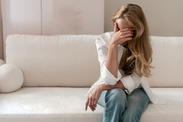 Mature woman sitting on couch with hand on head, dealing with headache and stress