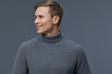 Stylish young man with short brown hair wearing a cozy gray turtleneck sweater, smiling to the...