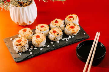 Delicious sushi rolls served on a black slate plate with a red background and dipping sauce