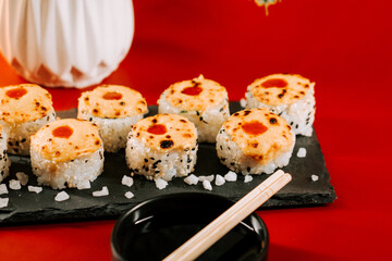 Sushi rolls on a black slate plate with vibrant red background and dipping sauce beside them