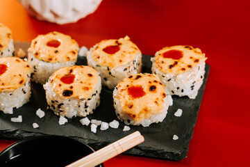 Delicious sushi rolls with melted cheese and spicy sauce on a black serving plate