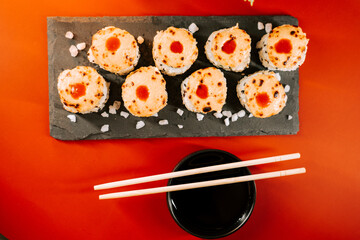 Delicious sushi rolls served on a black slate plate with chopsticks and dipping sauce