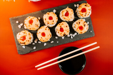 Sushi rolls with spicy sauce and dipping sauce on stone plate at a restaurant