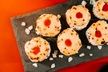 Unique sushi rolls with melted cheese and sauce on a black stone platter