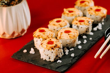 Sushi rolls with grilled topping served on a black plate in a vibrant setting