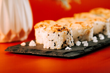 Delicious sushi rolls served on a black slate plate with salt on a vibrant red background