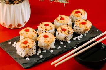 Sushi rolls with melted cheese and spicy sauce on a black stone plate