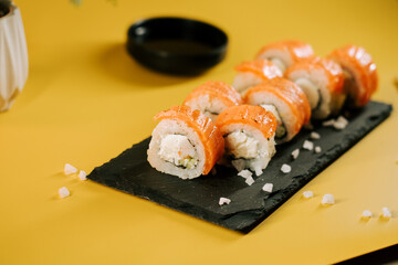 Sushi rolls arranged neatly on a black slate serving platter inspired by a vibrant yellow background