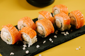 Fresh salmon sushi rolls served on a black stone plate with a bright yellow background