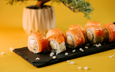 Fresh sushi rolls served on a black stone plate with a decorative plant in the background