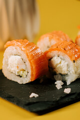 Sushi rolls with salmon and cream cheese on a black slate platter in a bright setting