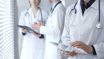 Medical professional using a digital tablet for patient care and data management, collaborating with doctors and healthcare workers in a modern clinic or hospital setting