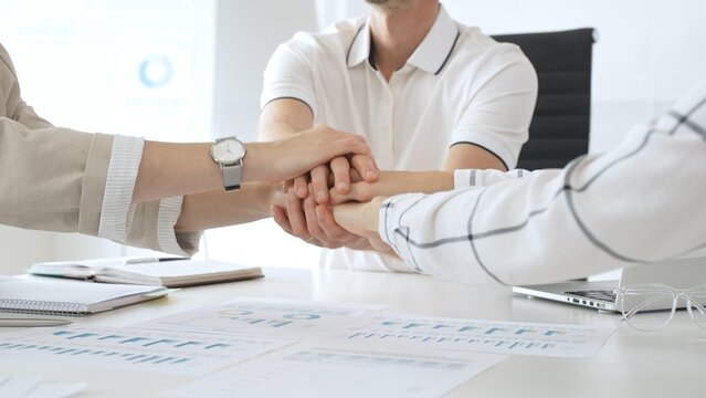 Business people team joining hands over workplace documents, symbolizing collaborative spirit and shared workplace success, close up view