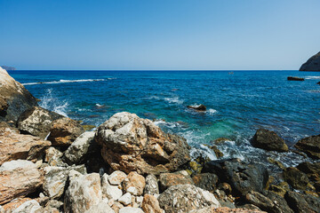 Endless blue waters embrace rugged rocks under a bright sun at a serene coastal escape