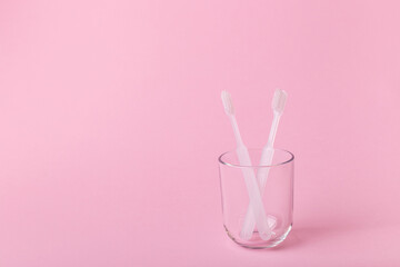 White toothbrushes in glass and vitamins on pink background. Oral care, gum and teeth health. Morning routine and health care.