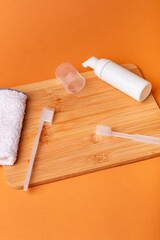 White toothbrushes on wooden desk, toothpaste and face towel from above on orange background. Oral care, gum and teeth health. Morning routine and dental care.