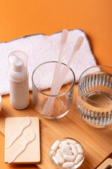 White toothbrushes in glass, dental floss, mouthwash on wooden desk, toothpaste and face towel on orange background. Oral care, gum and teeth health. Morning routine and dental care.