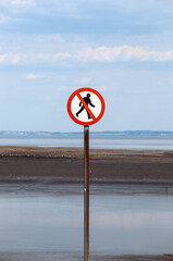 No pedestrians sign near the shore with a calm seascape and cloudy sky in the background
