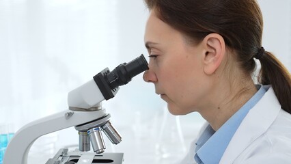 Female scientist examining samples through a microscope in a modern lab, conducting pharmaceutical research and developing treatments. Medicine, healthcare and science concept
