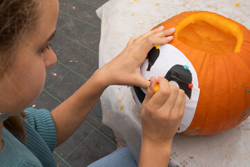 Young girl carefully decorating a pumpkin with a black and white design, using colorful pins and a marker, showcasing creativity and festive spirit in autumn crafting