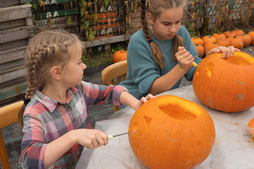 Two young girls engaged in pumpkin carving activity outdoors, showcasing creativity and teamwork while surrounded by autumn decorations and vibrant pumpkins