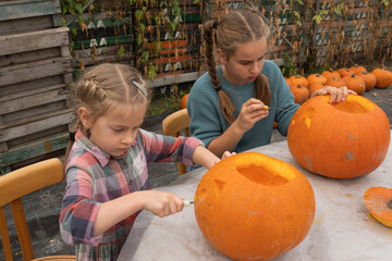 Two young girls, one with braids and the other with long hair, are carving pumpkins together outdoors, showcasing creativity and teamwork in a festive autumn setting