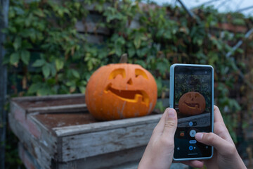 Person capturing photo of carved pumpkin with smartphone, showcasing autumn decorations and rustic wooden background, highlighting seasonal festivities and creativity