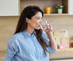 Portrait of a young woman gettyng ready for work drinking a glass of water for hydration standing...
