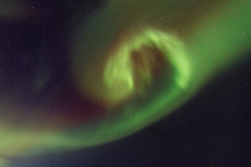 Vibrant aurora borealis displays swirling green and purple lights across a starry night sky,...