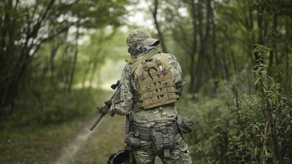 Camouflaged army soldier with AR15 carbine on a mission. Sneaking through a thick green forest. Military recon