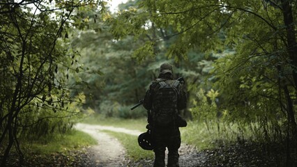 Camouflaged army soldier with AR15 carbine on a mission. Carefully sneaking through a thick green forest. Military recon