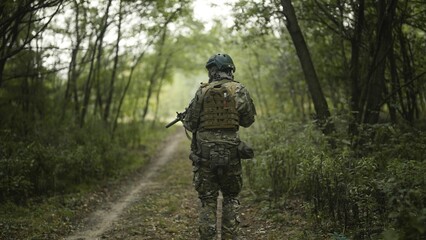 Camouflaged army soldier with AR15 carbine on a mission. Traversing the rough terrain of trees and bushes. Military recon