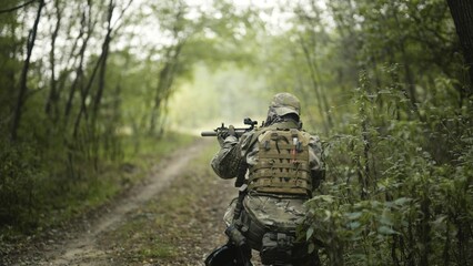 Camouflaged army soldier with AR15 carbine on a mission. Standing still and taking aim with the rifle. Military recon