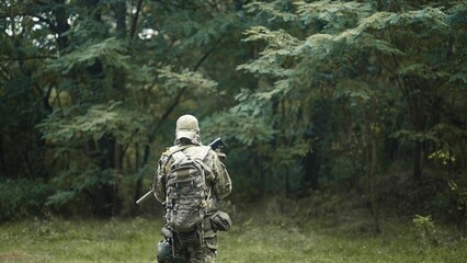 Camouflaged army soldier with AR15 carbine on a recon mission. Traversing the rough terrain of bushes. Military recon