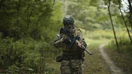 Camouflaged and masked army soldier with AR15 carbine on a war recon mission. Walking through the forest. Military recon