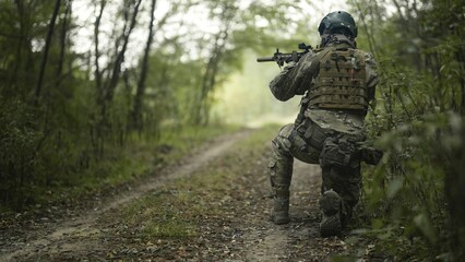 Camouflaged army soldier with AR15 carbine on a recon mission. Sitting still hidden in bushes and aiming. Military recon