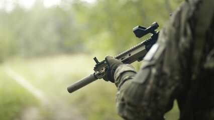 Camouflaged and masked army soldier with AR15 carbine on a war recon mission. Walking through a grass field. Military recon
