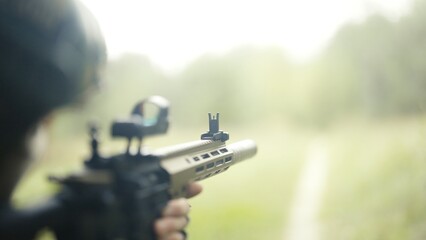Camouflaged and masked army soldier with AR15 carbine on a war recon mission. Standing on a grass field and aiming. Military recon