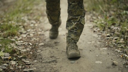 Camouflaged and masked army soldier on a war recon mission. Close-up feet walking on a dirt path. Military recon