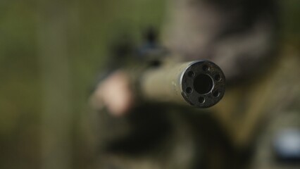Camouflaged army soldier with AR15 carbine. Rifle with a collimator aiming at the camera. Selective focus. Military war recon